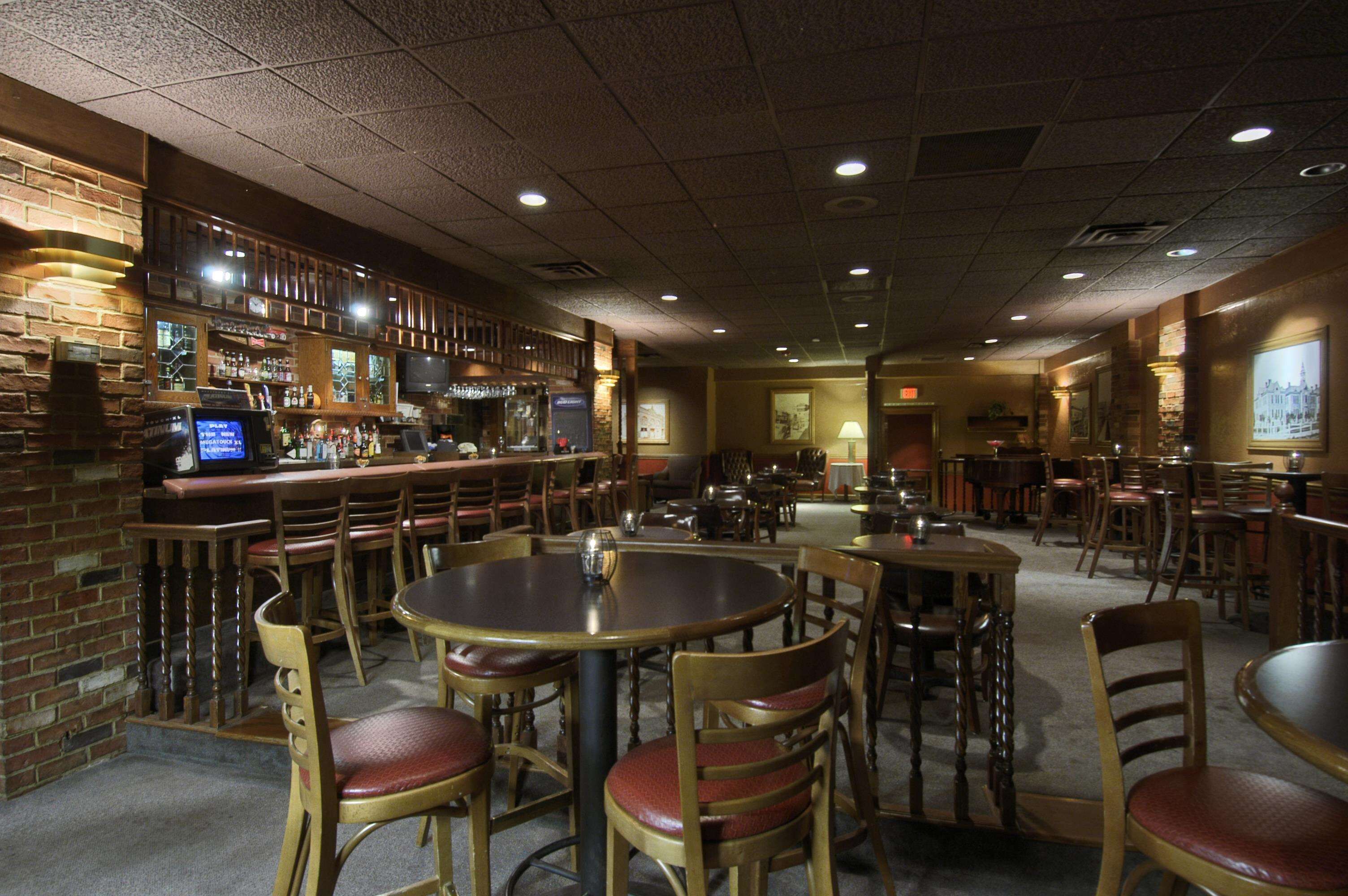 Un restaurante con varias mesas y sillas, una zona de bar con mostrador y estantes llenos de botellas, y una pantalla de televisión.