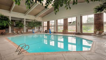 An indoor swimming pool with clear blue water, surrounded by lounge chairs and a brick wall.