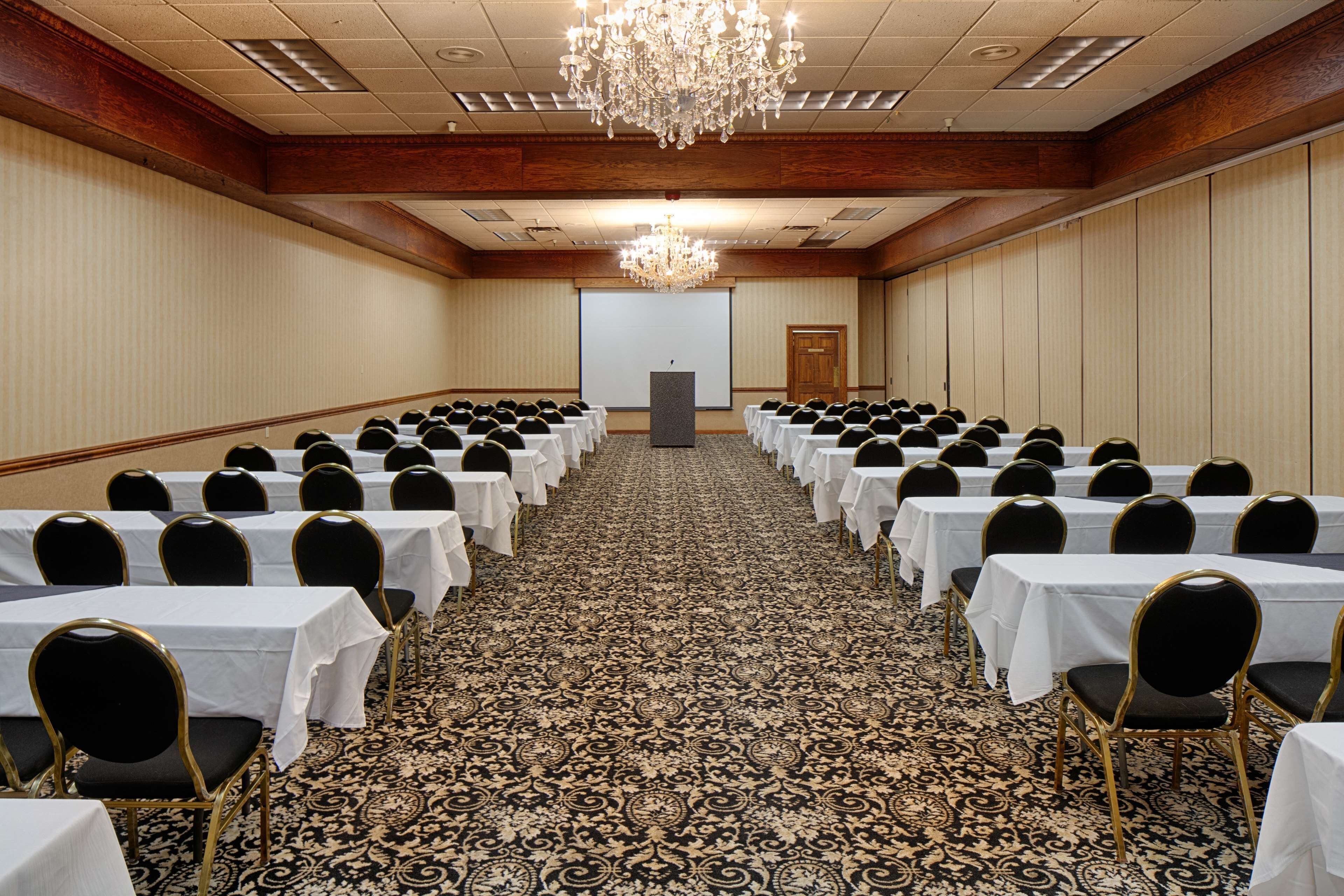 Un salón de conferencias con filas de mesas y sillas, suelo alfombrado y un candelabro.