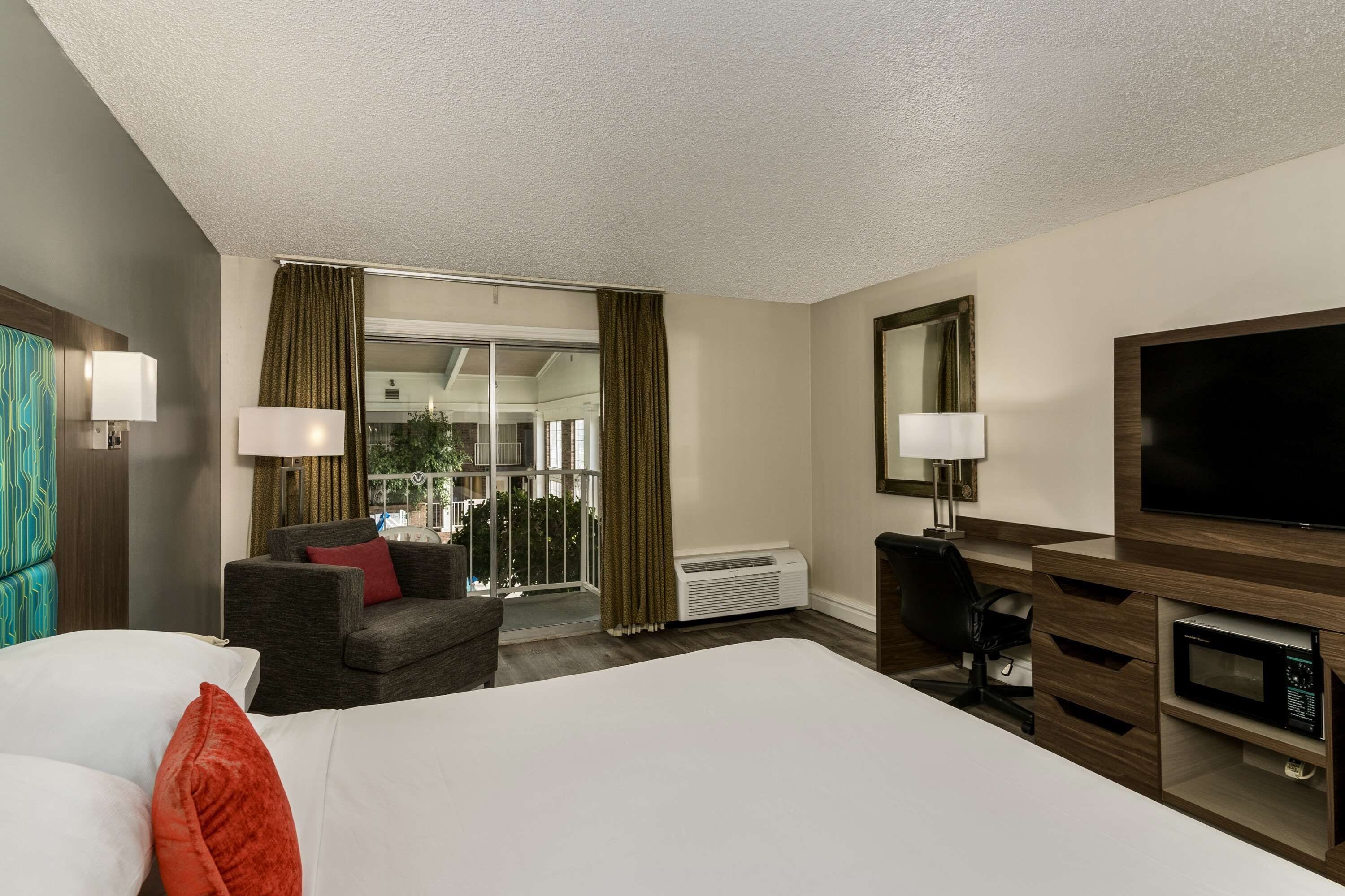 Une chambre d’hôtel avec un lit, un canapé, une télévision, un bureau et une fenêtre avec des rideaux.