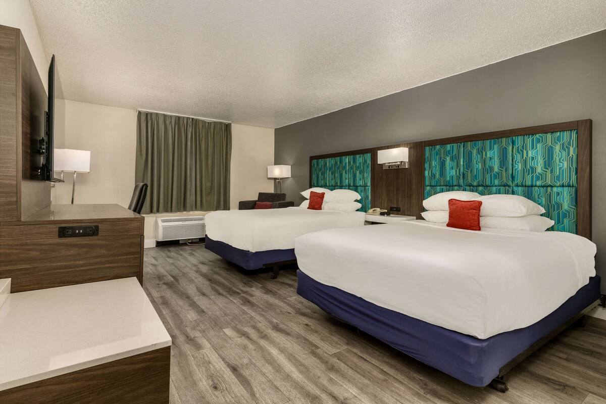 A hotel room with two beds, a TV, a desk, and a lamp.