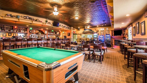 A bar area with pool tables, seating, and a variety of bottles on shelves.