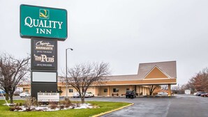 A Quality Inn with a signboard, a parking lot, and a building with a brown roof.