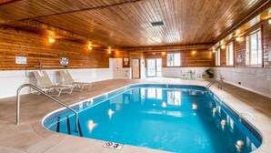 An indoor swimming pool with wooden walls and ceiling, lounge chairs, and a poolside table.