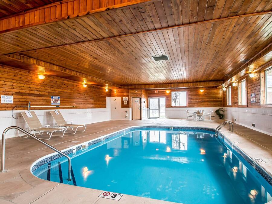 Une piscine intérieure aux murs et au plafond en bois, dotée de chaises longues et d’une table située au bord du bassin.