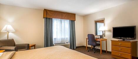 A hotel room with a large bed, a desk with a chair, a television, and a dresser.