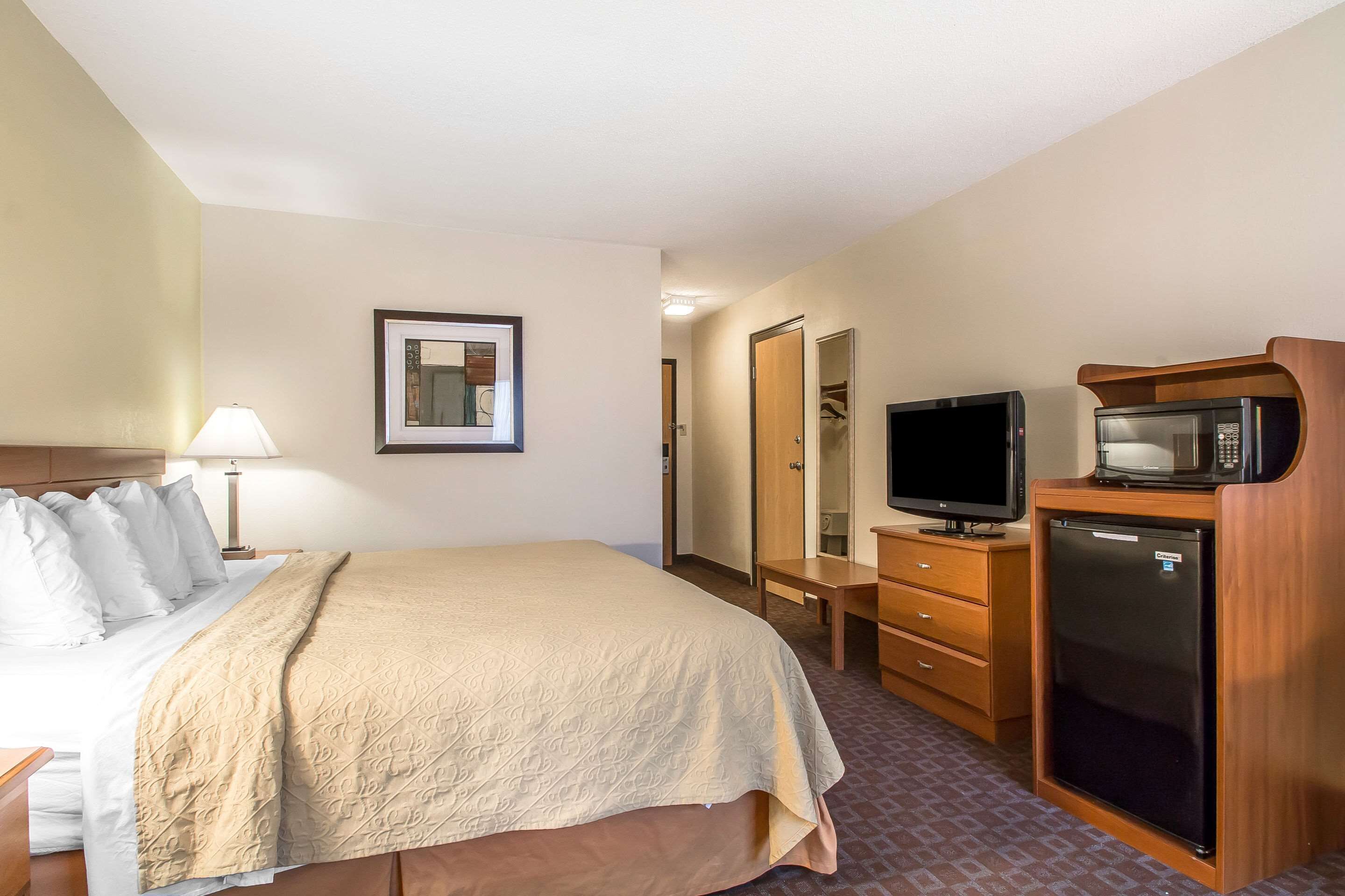 A hotel room with a bed, a television, a microwave, a dresser, and a mirror.
