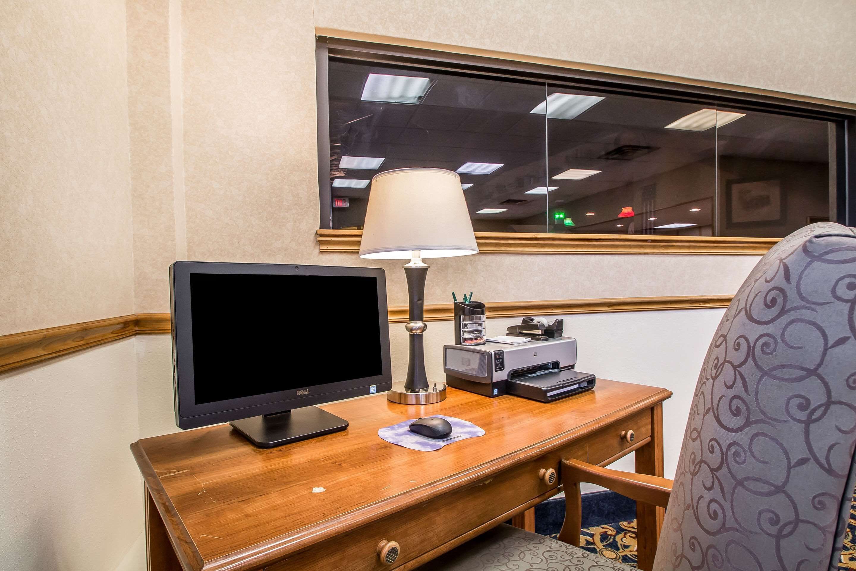 A hotel desk with a computer monitor, a lamp, a printer, and a chair.