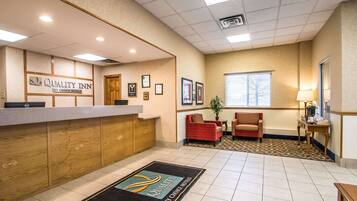 A hotel reception area with a reception desk, a red sofa, a small table with a lamp, and framed certificates on the wall.