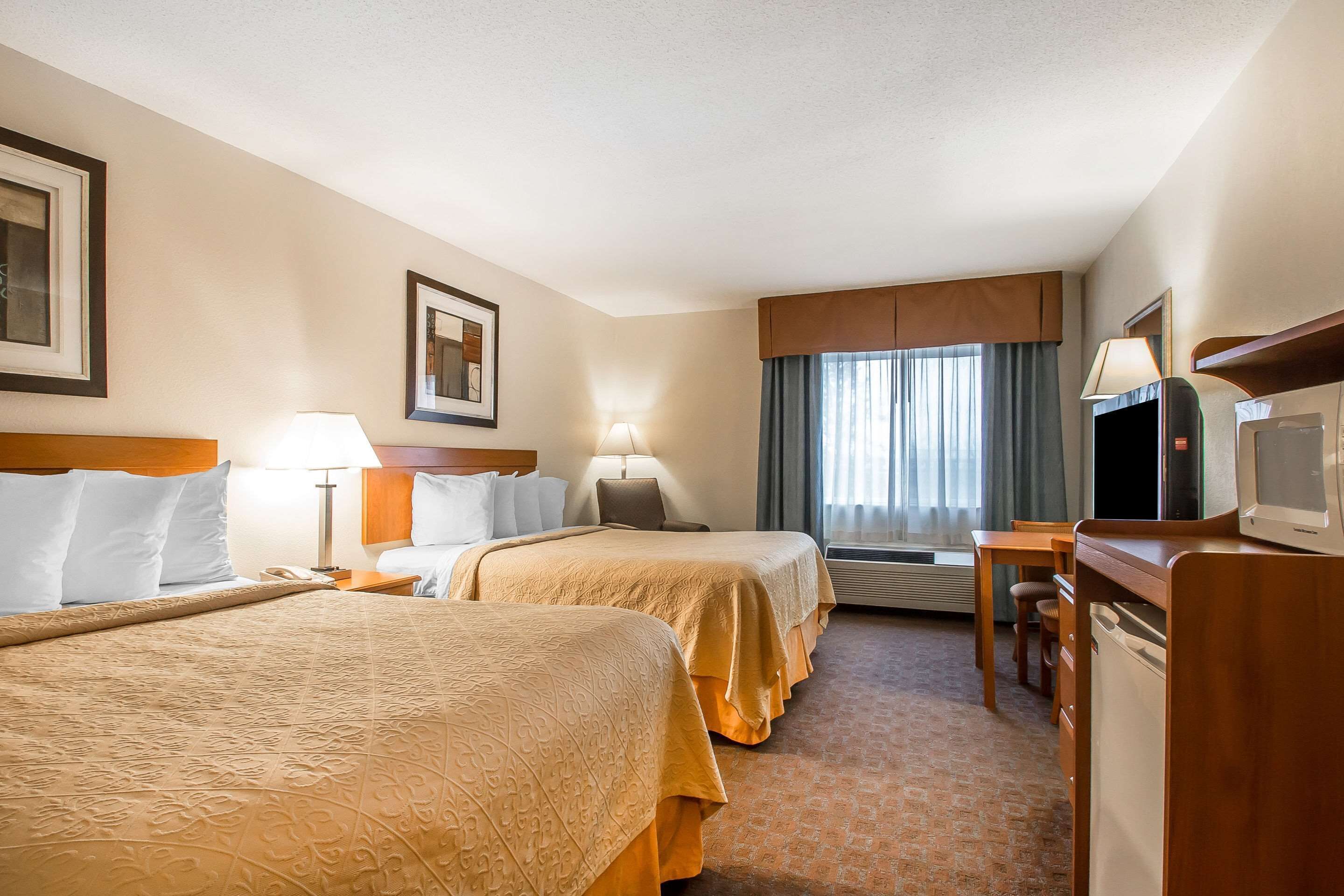 A hotel room with two beds, a desk, a television, and a window with curtains.