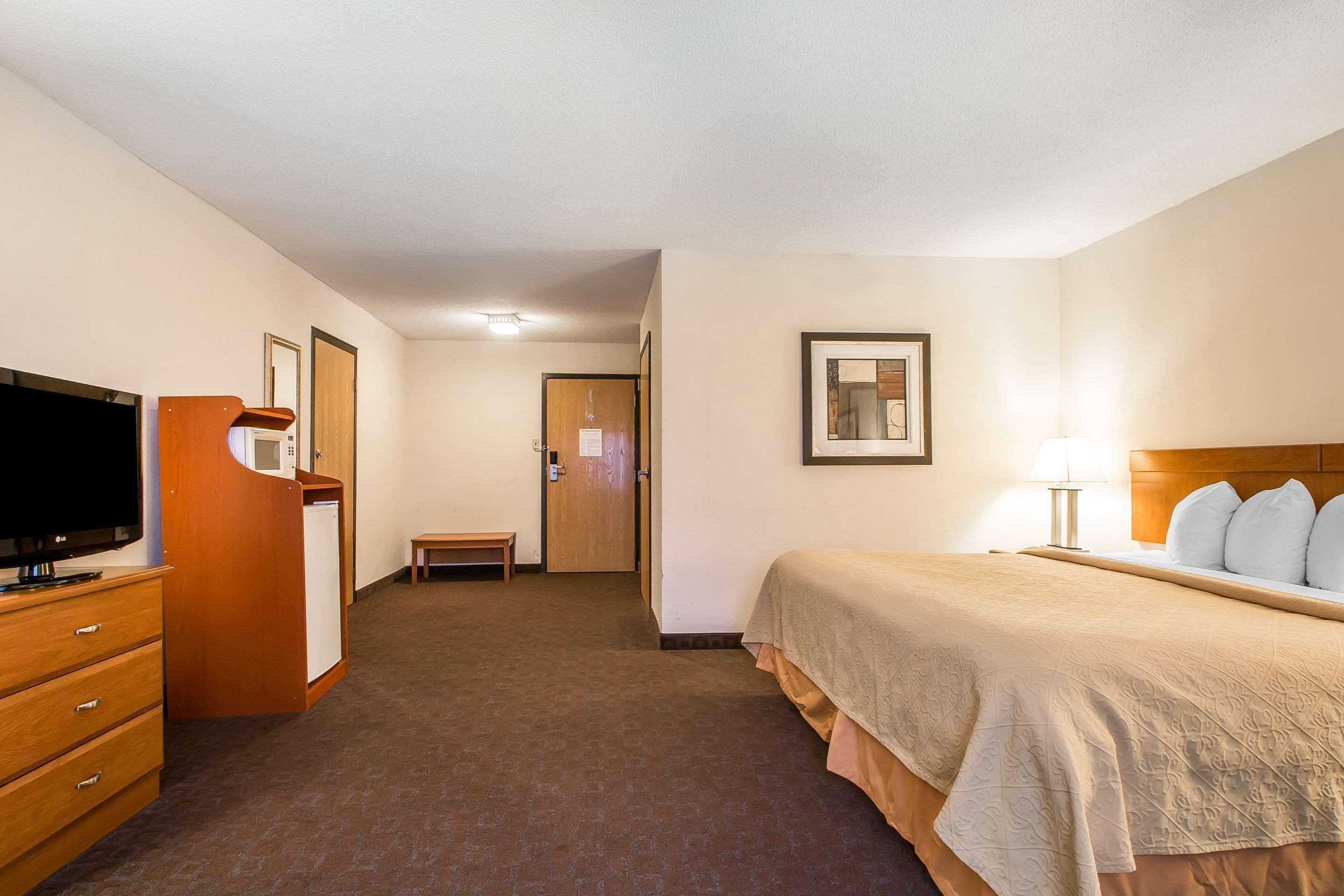 A hotel room with a bed, a television, a desk, and a door leading to a hallway.
