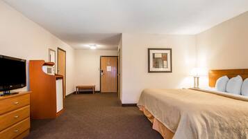 A hotel room with a bed, a television, a desk, and a door leading to a hallway.