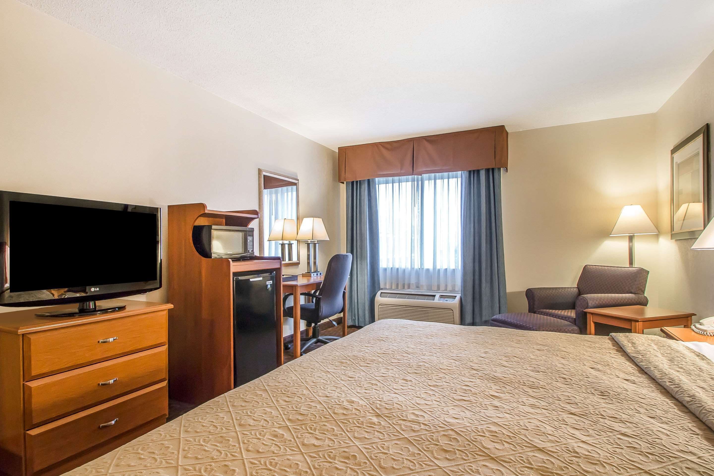A hotel room with a large bed, a desk with a computer, a television, and a chair.