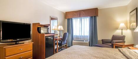 A hotel room with a large bed, a desk with a computer, a television, and a chair.