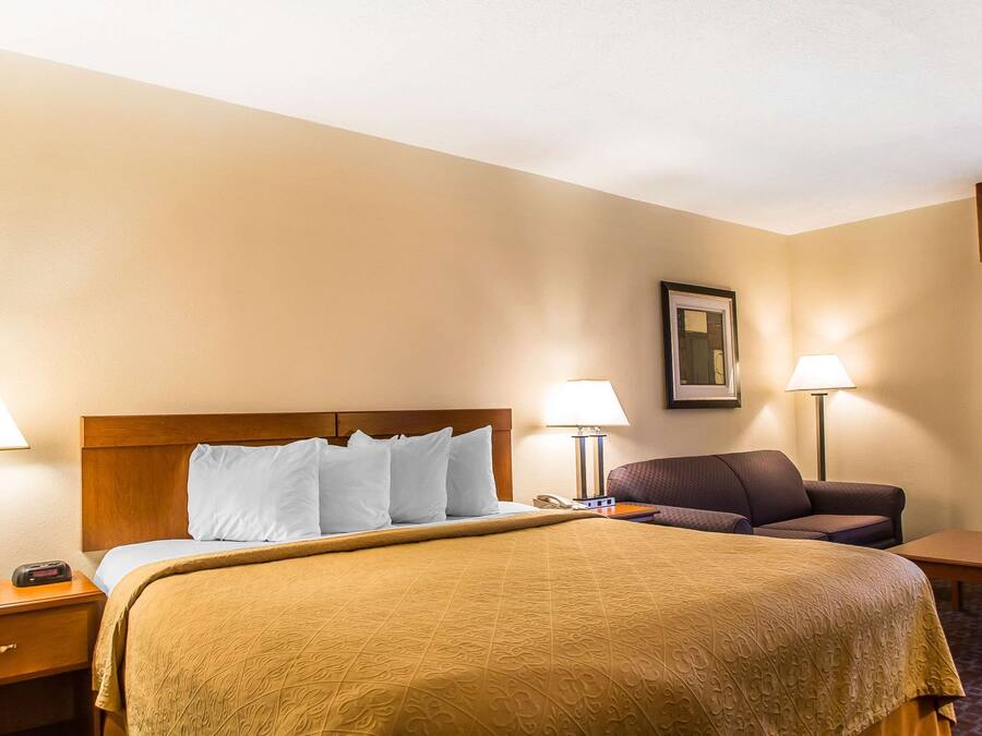 Habitación de hotel con una cama grande, dos mesitas de noche con lámparas, una silla y una pequeña mesa.