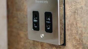A metal switchboard with a shavers-only label and two electrical outlets, one labeled 230V and the other 115V.