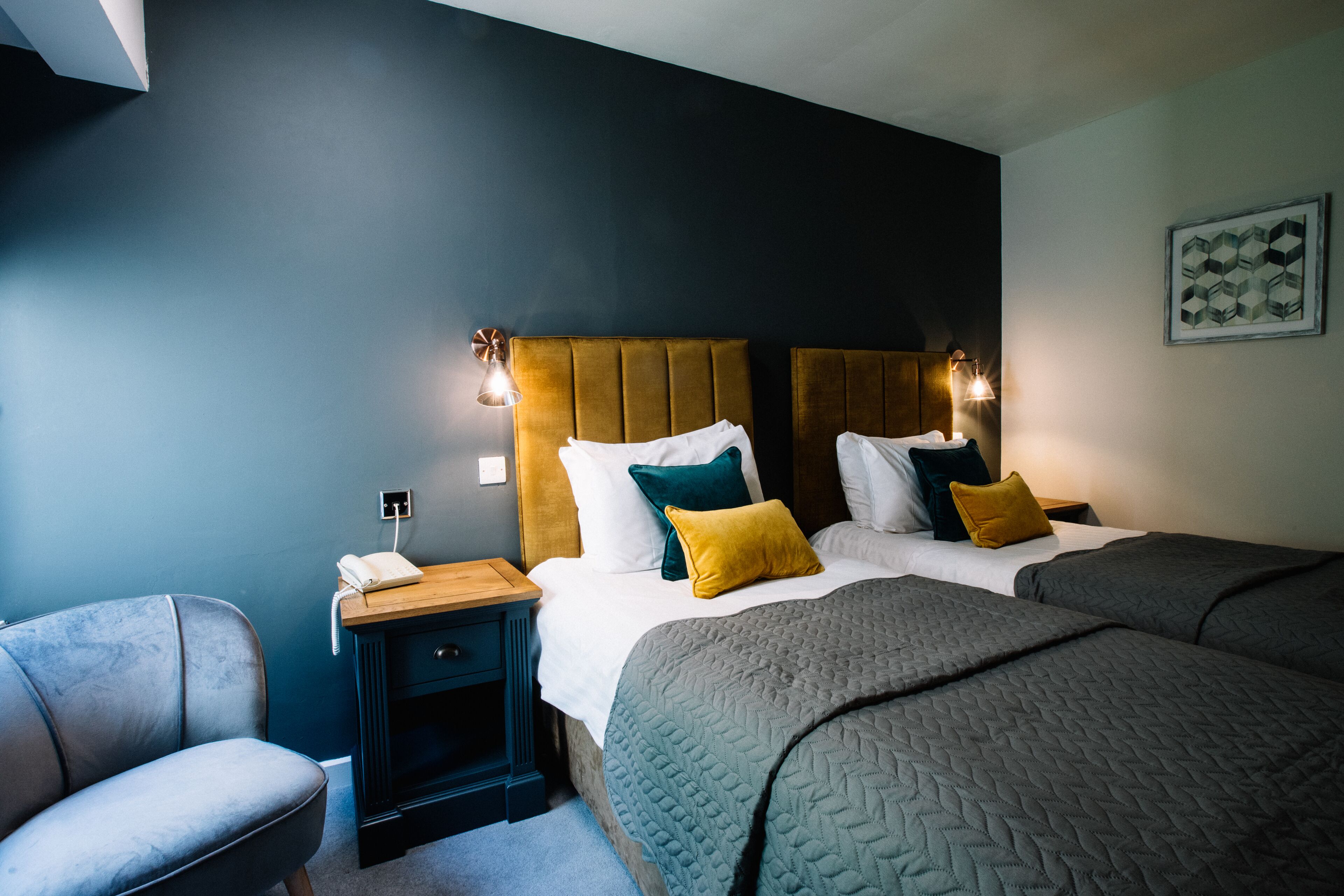 Une chambre d’hôtel comprenant un lit, des tables de chevet, une chaise et un luminaire fixé au mur.