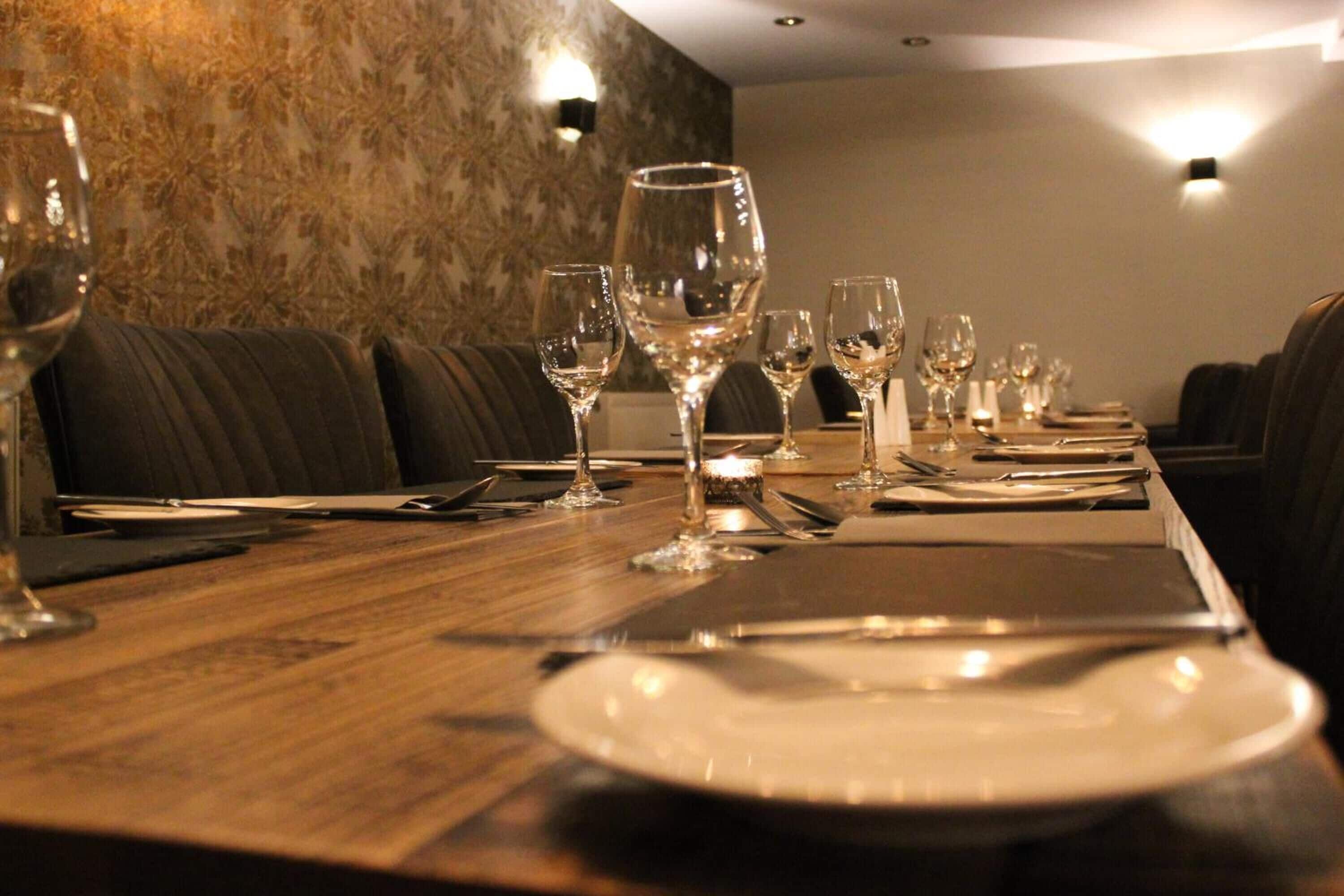A dining table set with wine glasses, plates, and cutlery in a restaurant with a patterned wall and cushioned seating.