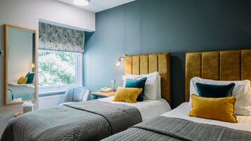 A hotel room with two beds, a large window, a mirror, and a bedside table with a lamp.