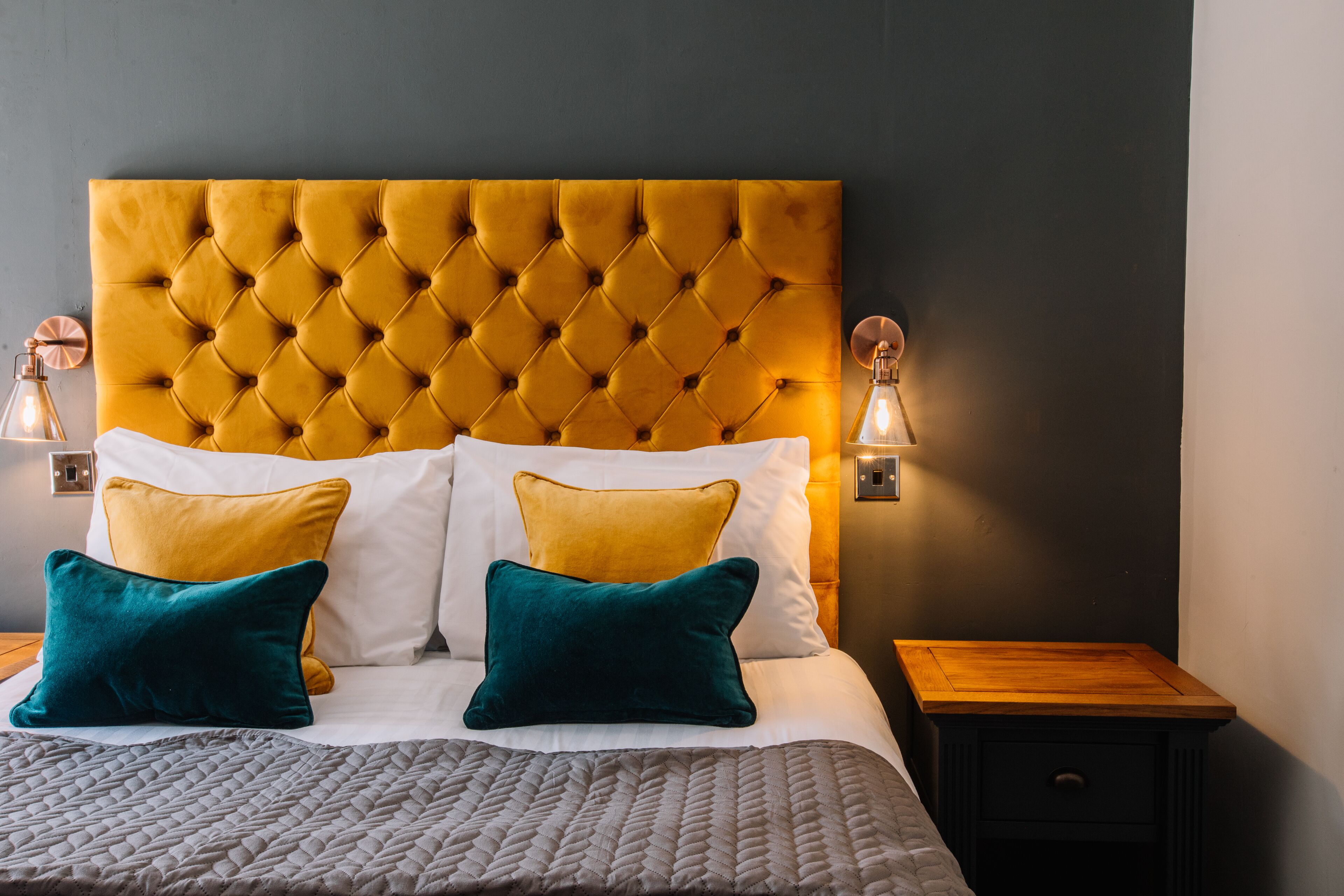 A neatly made bed with a tufted headboard, two bedside tables, and wall-mounted lamps.