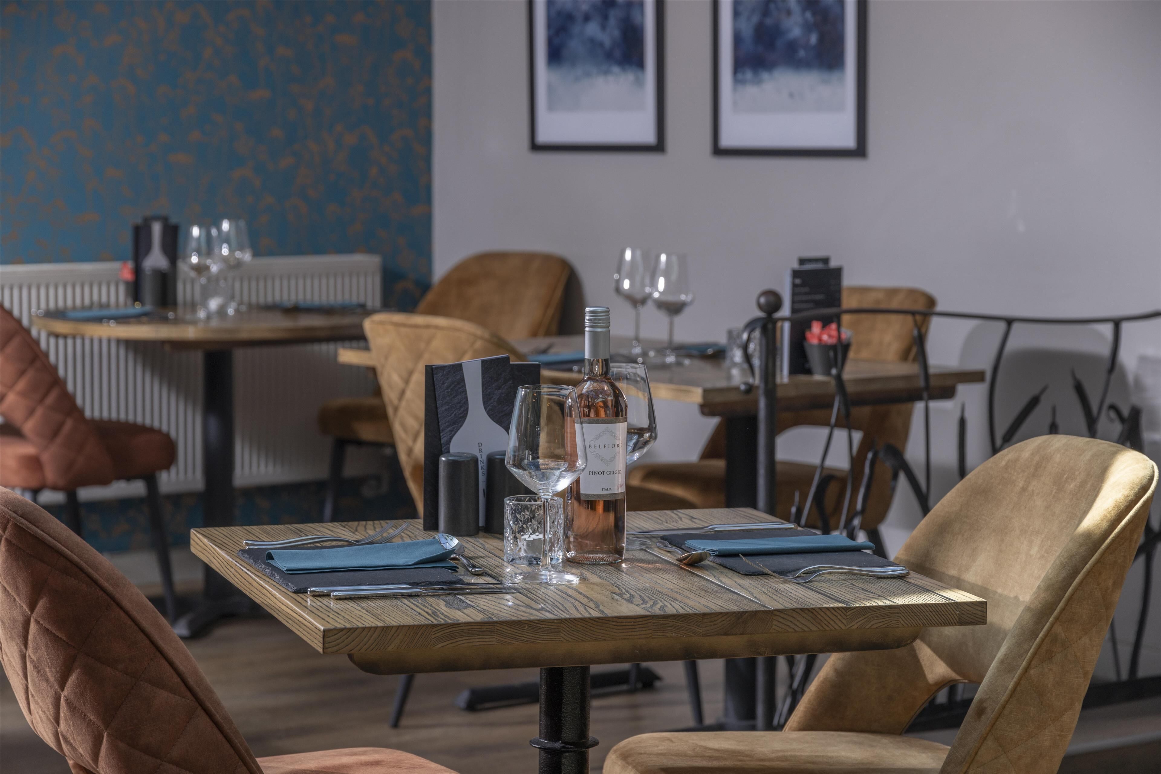 A dining area with tables set for two, featuring a bottle of wine, glasses, and neatly arranged cutlery.