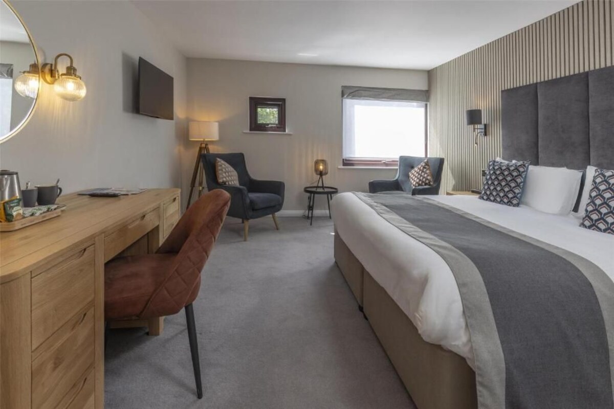 A hotel room with a bed, a desk, a chair, a lamp, and a television.