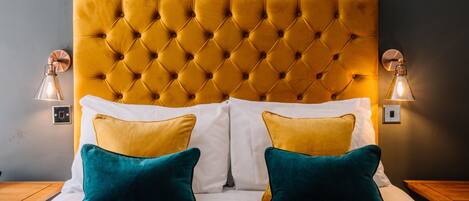 A bed with a tufted headboard, white and yellow pillows, and a grey quilt.