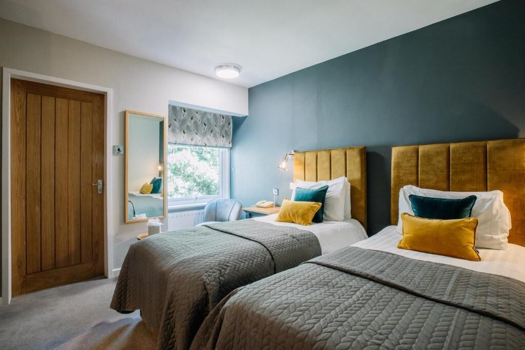 Habitación de hotel con dos camas, una puerta de madera, un ventanal con vistas y un espejo.