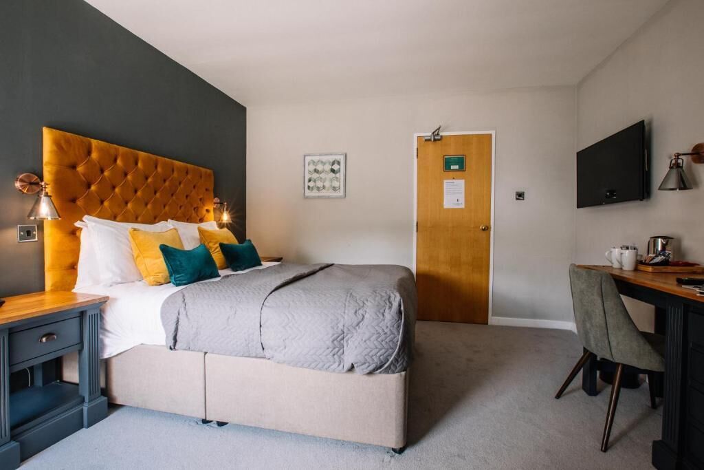 A hotel room with a large bed, a desk, a chair, a television, and a door.