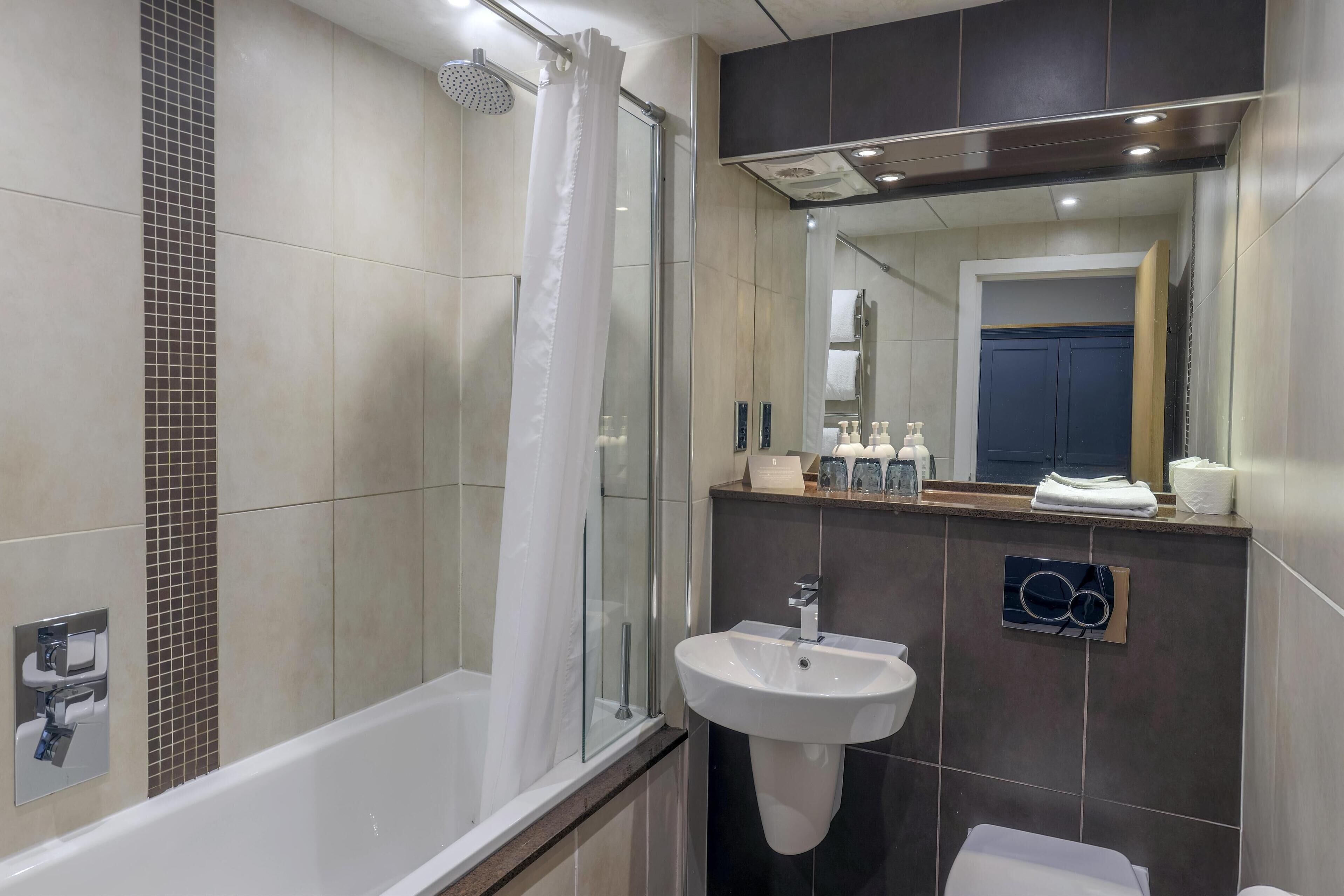 A modern bathroom with a glass-enclosed shower, a white bathtub, a sink, and a mirror above the sink.