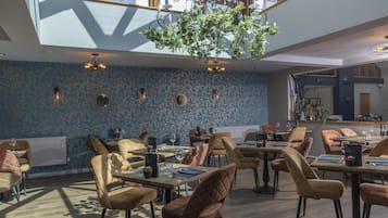 A dining area with round tables, cushioned chairs, and a ceiling garden.