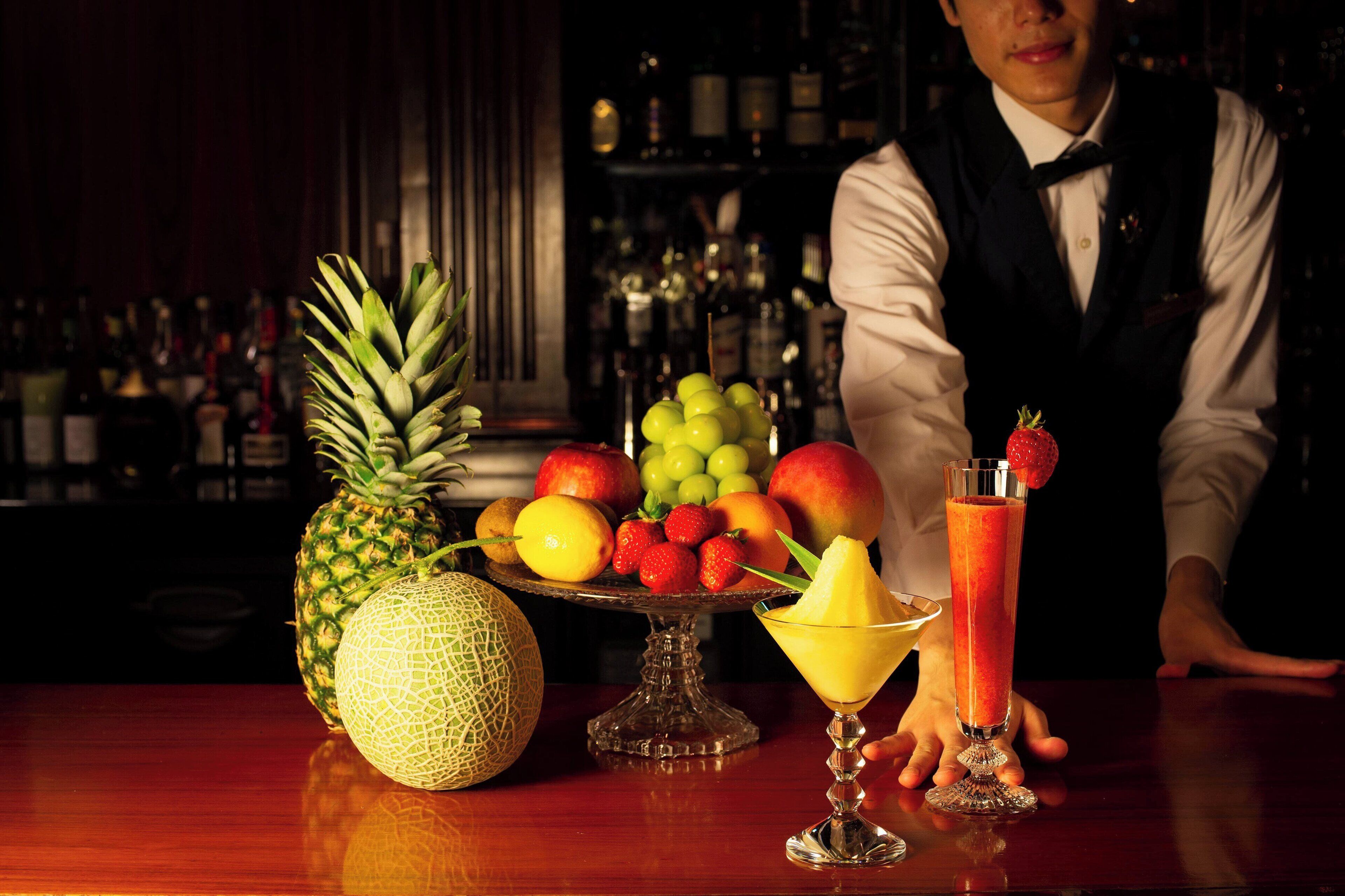 A bar setting with a fruit display, a cocktail, and a bartender.