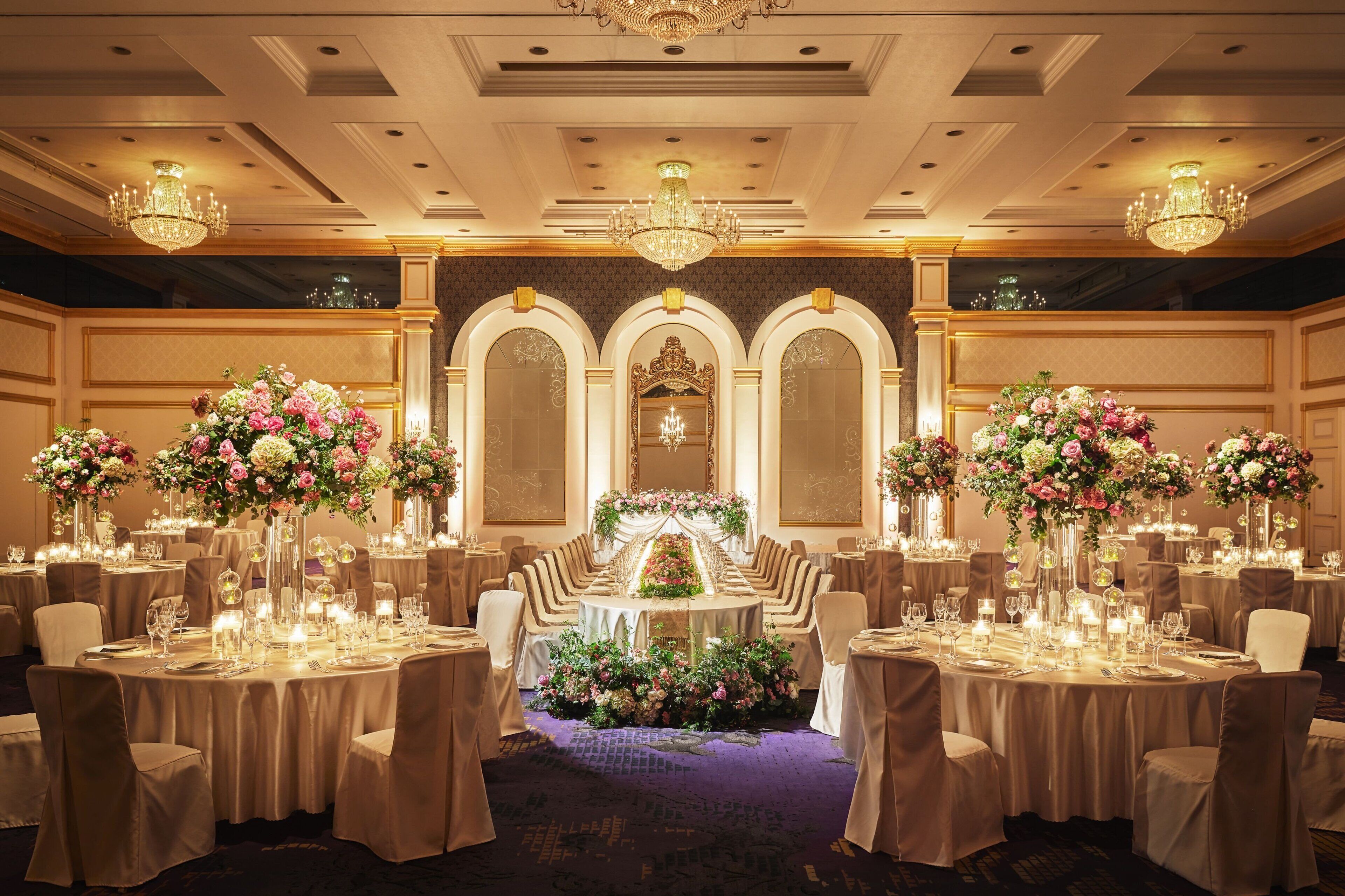 Un salón de banquetes con mesas redondas, candelabros y centros de mesa florales.