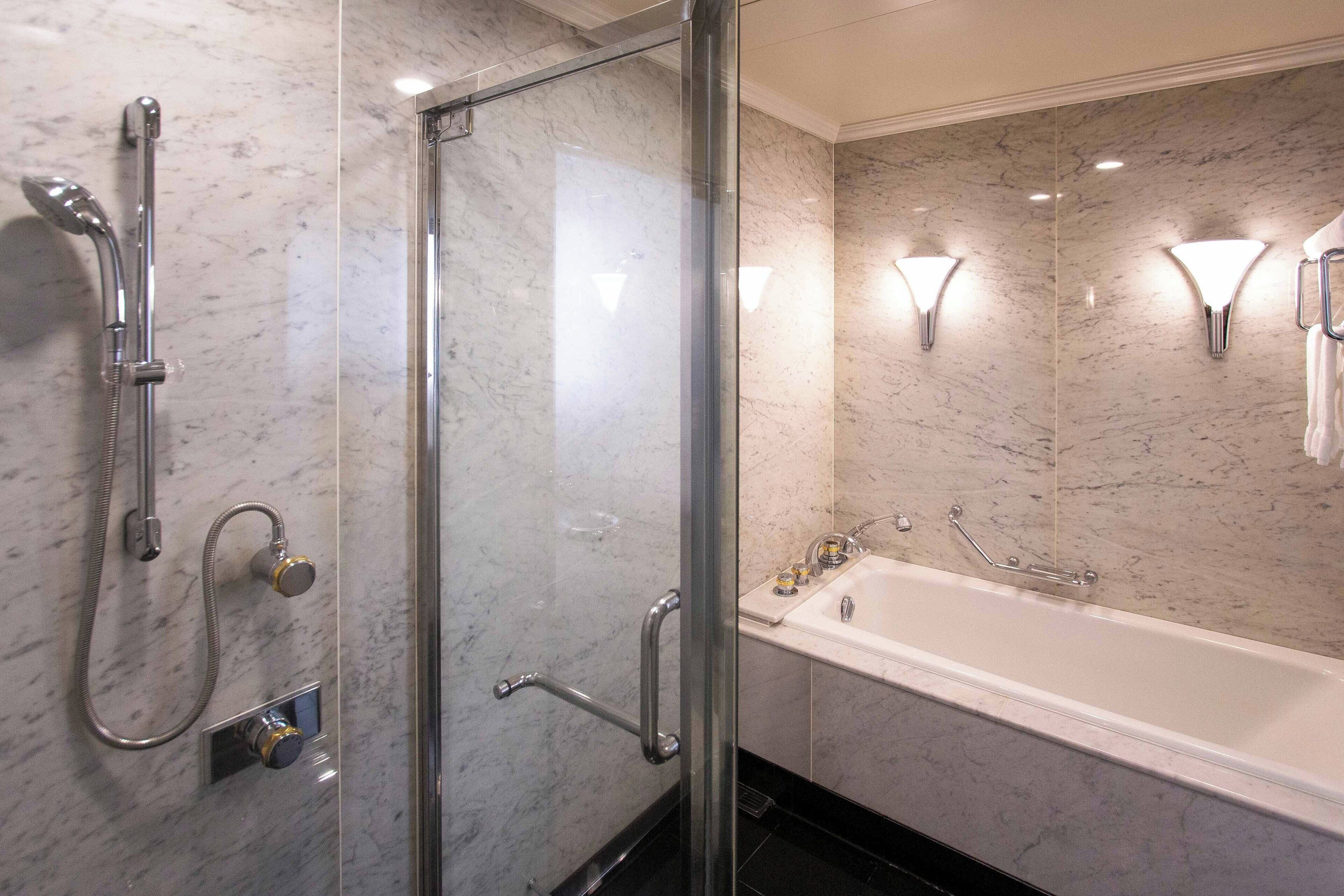 A modern bathroom with a glass-enclosed shower, a white bathtub, and marble walls.