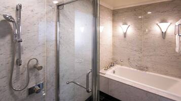 A modern bathroom with a glass-enclosed shower, a white bathtub, and marble walls.