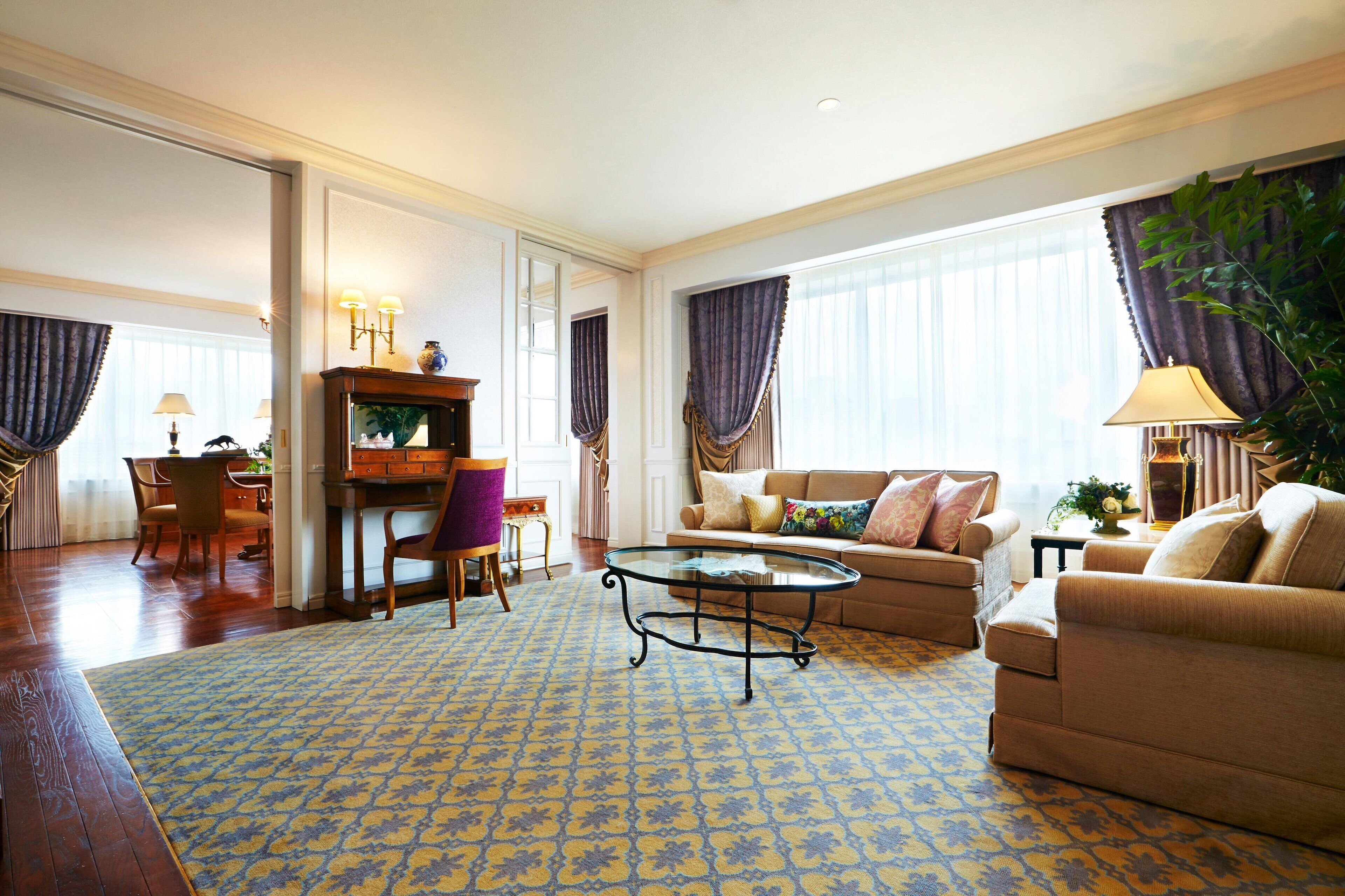 A spacious living room with a patterned rug, a sofa, a coffee table, and a dining area with chairs and a table.