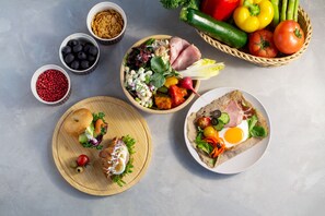 Ett urval av olika matvaror, inklusive sallader, bröd och grönsaker, som står uppradade på ett bord.