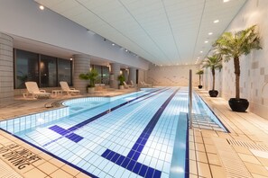 En modern inomhuspool med tydliga markeringar för banorna, solstolar och krukväxter.