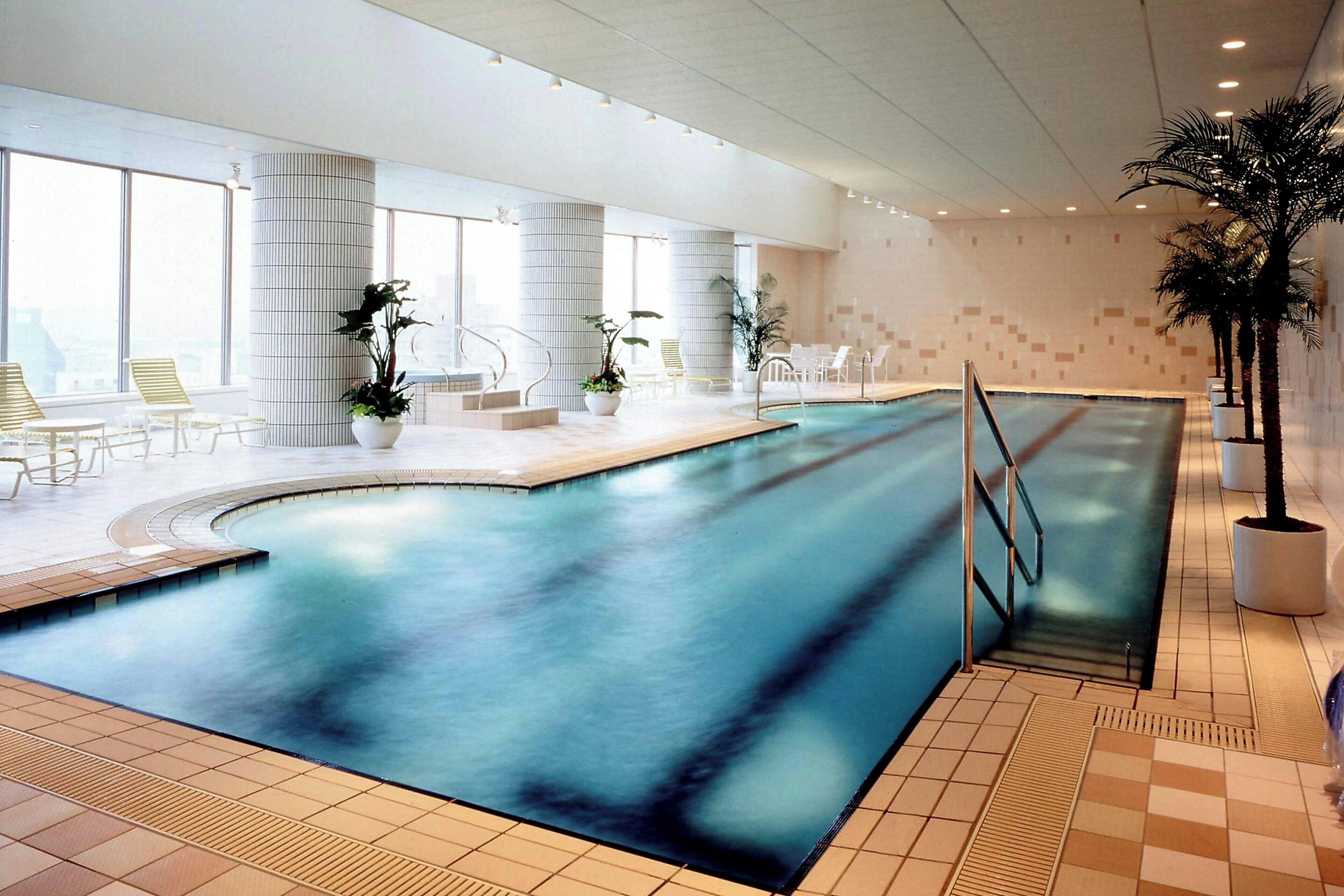 An indoor swimming pool with clear water, surrounded by lounge chairs and potted plants.
