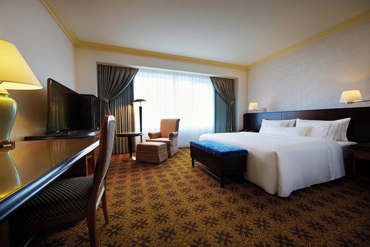 A hotel room with a bed, a desk, a chair, a TV, and a window with curtains.