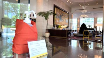 A hotel lobby with a reception desk, a large painting, a chandelier, and a red object on display.