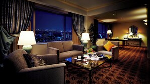 Habitación de hotel con vistas a la ciudad, dos sofás, una mesa de centro y un área de comedor con lámpara y mesa.
