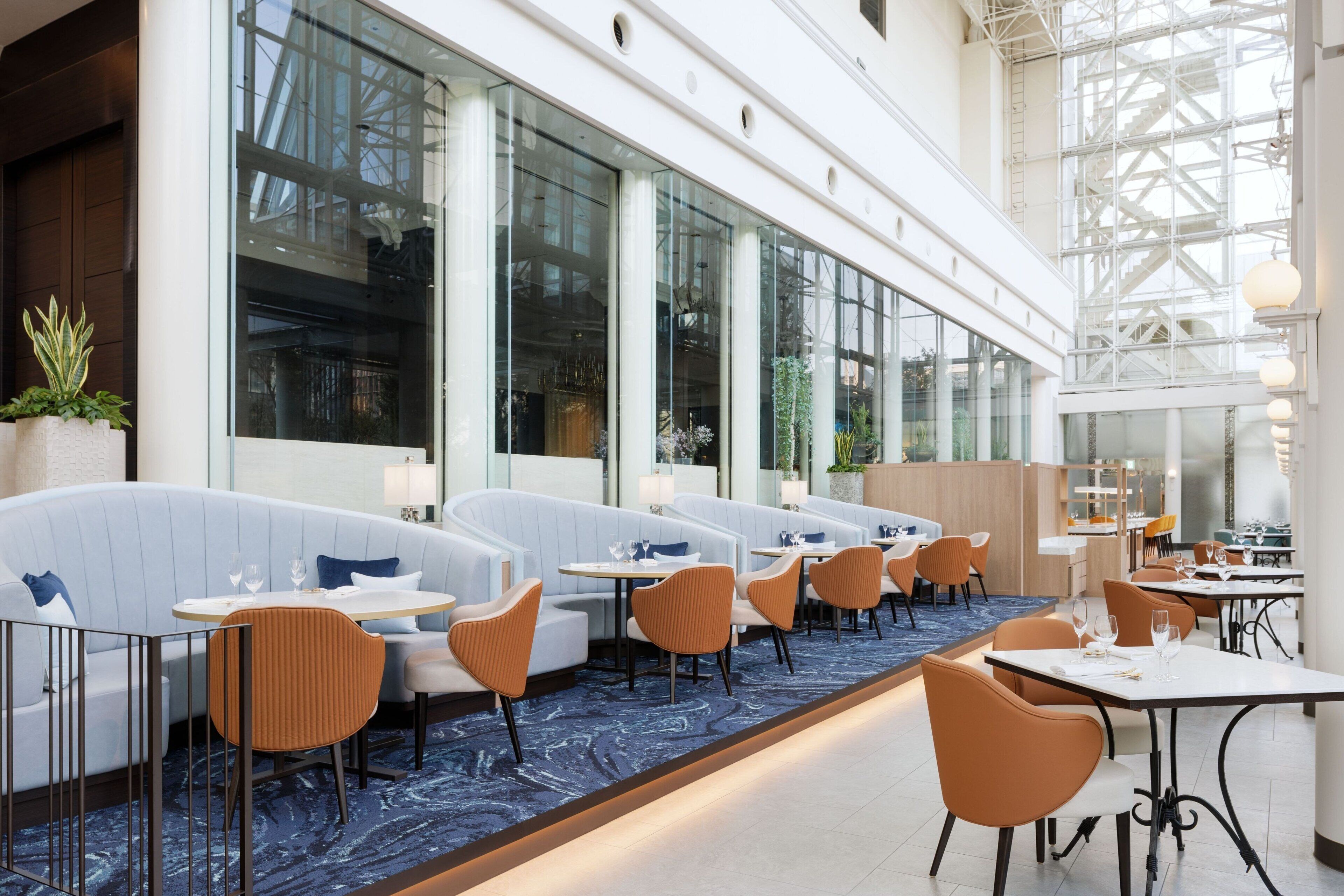 Un restaurante moderno con mesas a lo largo de las paredes, ventanas amplias y una alfombra azul.