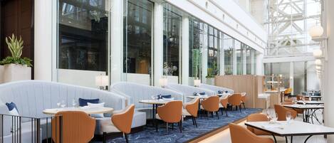 Un restaurante moderno con mesas a lo largo de las paredes, ventanas amplias y una alfombra azul.