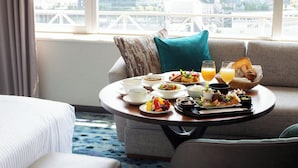 A dining table with breakfast items, a sofa, and a view of the cityscape through large windows.