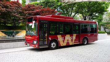 A red bus with "The Westin Osaka" branding parked on a paved area with a fountain and trees in the background.