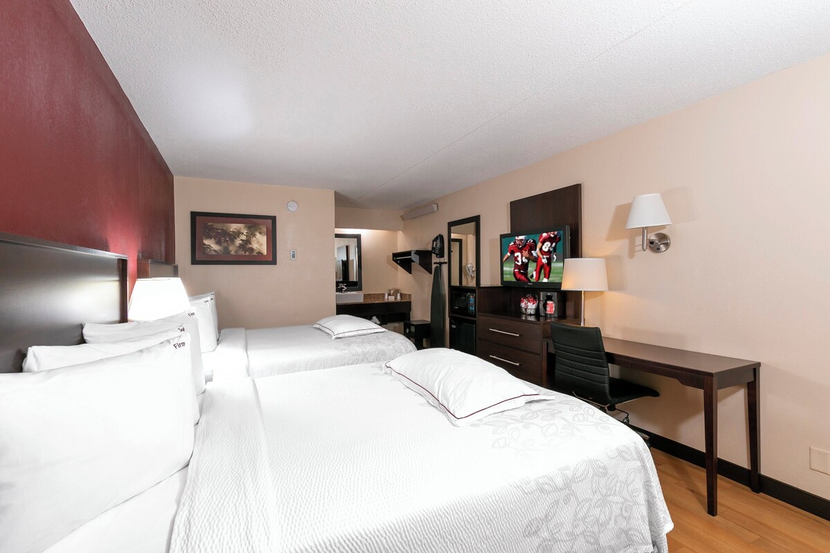Una habitación de hotel con dos camas, un escritorio, una silla, un televisor y una lámpara.