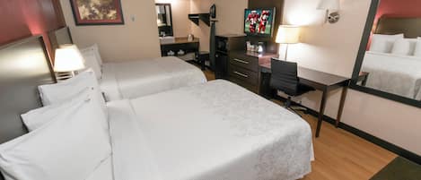 Habitación de hotel con dos camas, un escritorio, televisor, espejo y zona de baño.