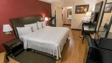 A hotel room with a bed, bedside table, lamp, and a desk with a chair.