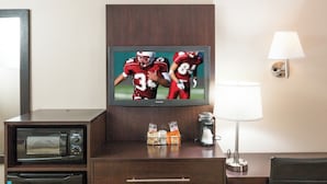 A hotel room with a television displaying a football game, a desk with a lamp, a microwave, and a refrigerator. - Red Roof Inn PLUS+ Ann Arbor - U of Michigan North (Ann Arbor)